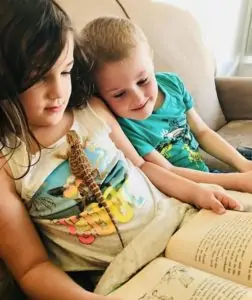 two kids sitting on a couch reading a book together