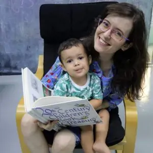 a picture of a mom holding a small child on her lap sitting in a chair reading a book