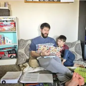 an image of a father sitting on a couch reading a book to a boy