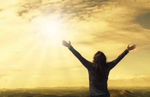 an image of a person standing outside raising their arms in the sun