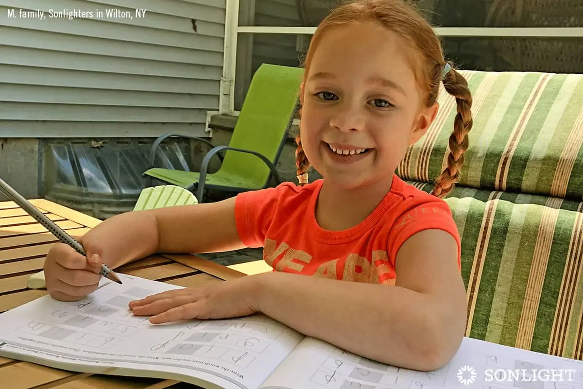 a little girl smiling and doing school work