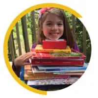 little girl smiling and holding a stack of books up to her chin