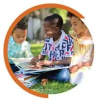 three kids reading a book together outside in the grass