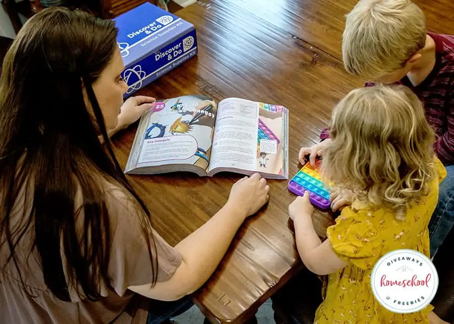 A mom and two children looking at the Sonlight Discover and Do science experiment book and doing a hands-on activity 