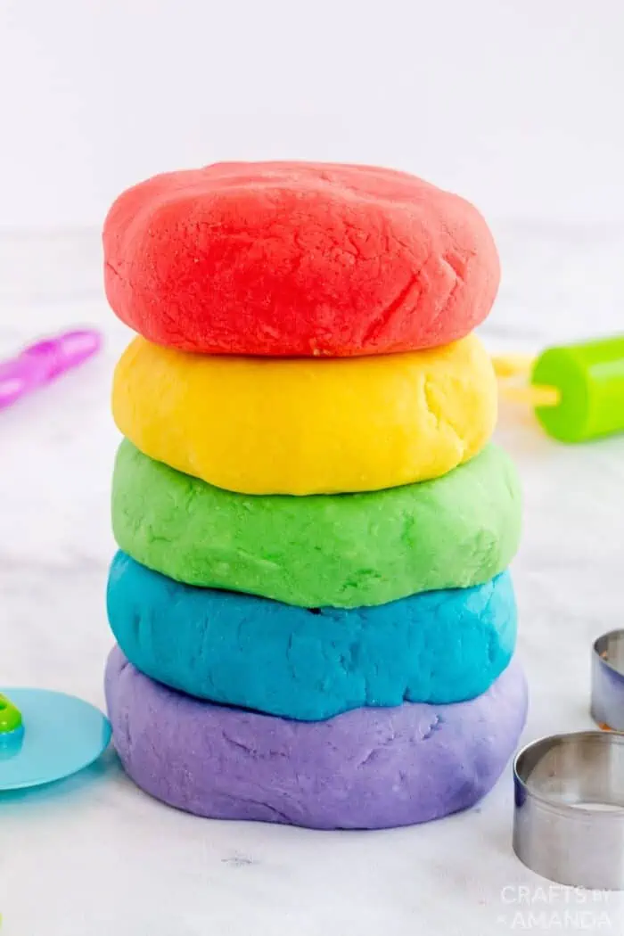 stack of colorful playdough on a counter with cutting tools. 