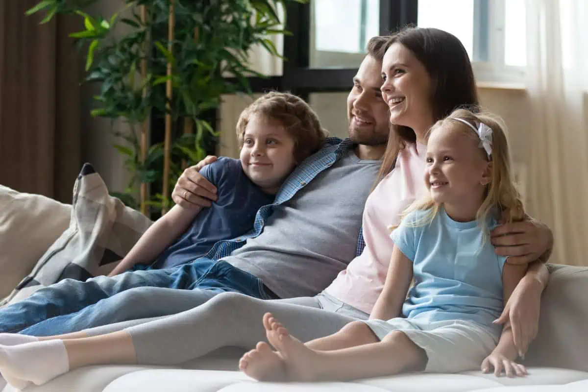 Family on the couch together smiling.  Looking to left and watching something together