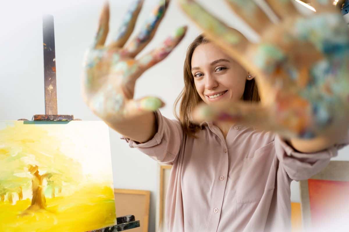 art therapy activities shows a teen holding up her hands with paint and smiling