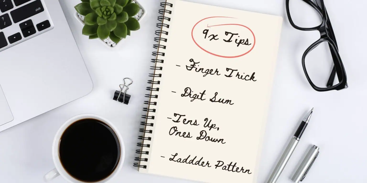 Desktop scene with a computer edge, coffee cup, pen, and small plant. In the center, an open notebook shows the title ‘9x Tips’ circled, with four tricks listed underneath: Finger Trick, Digit Sum, Tens Up Ones Down, and Ladder Pattern.